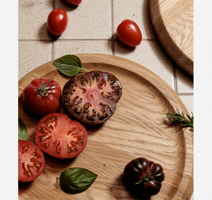 Wooden plate with sliced and whole tomatoes on a tiled surface