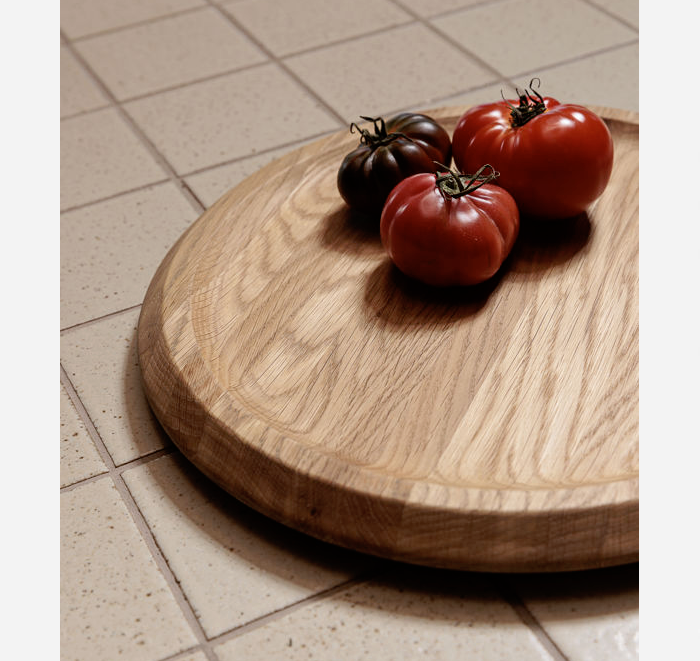 Three tomatoes on a wooden cutting board with a tiled floor background