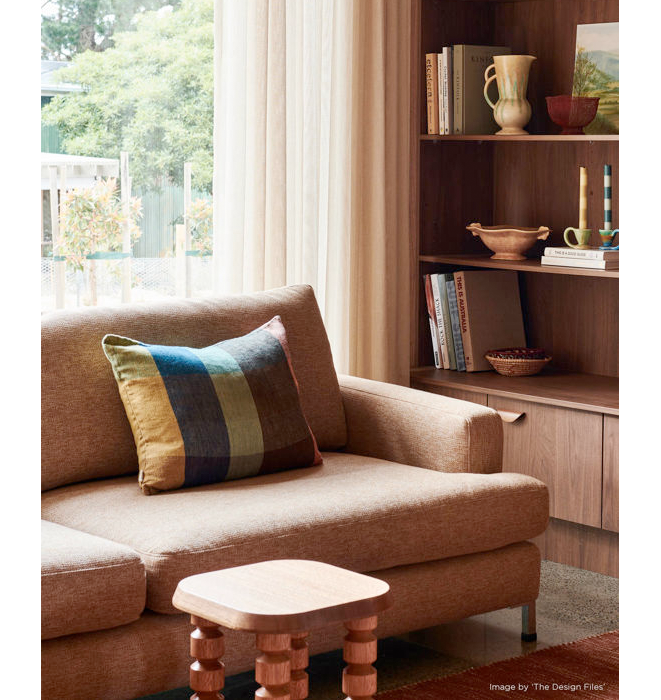 Brown sofa with a colorful pillow in a room with a bookshelf and window.