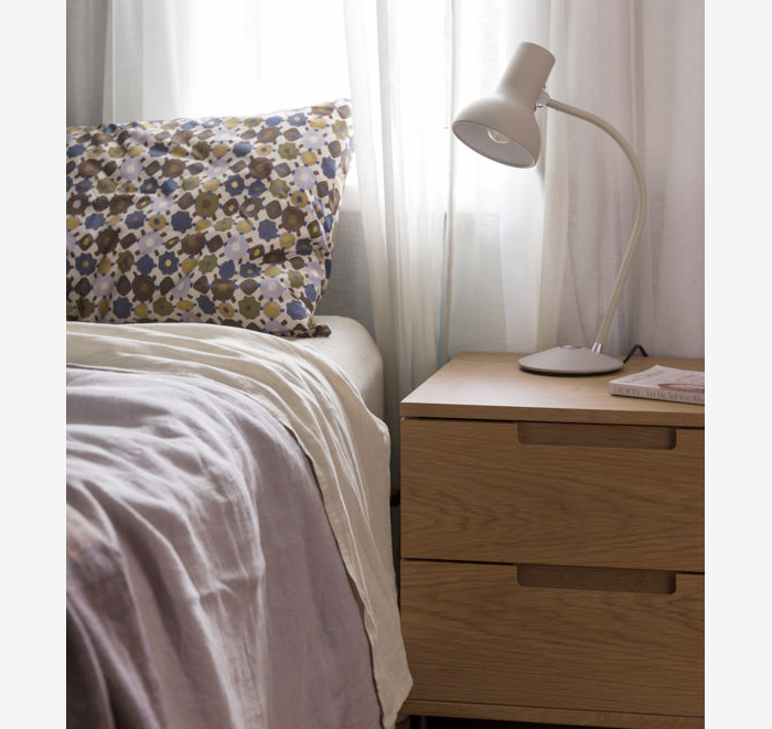 Bedroom scene with a bed and wooden nightstand featuring a lamp.