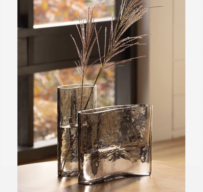 Two vases with decorative grasses on a wooden surface.