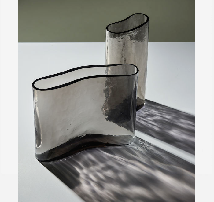 Two modern glass vases on a reflective surface with a neutral background