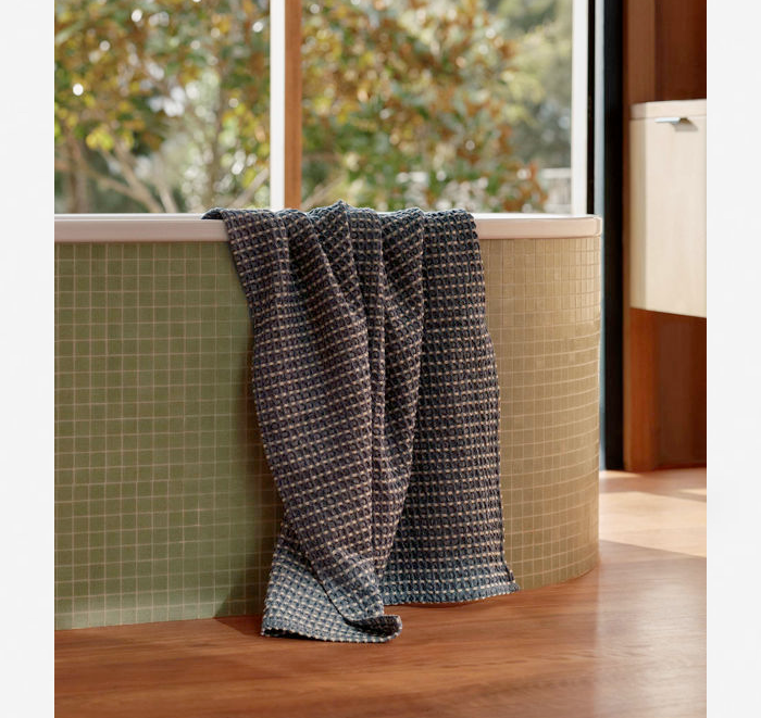 Gray towel draped over a bathtub with green tiled walls and a window in the background