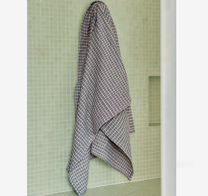 Textured towel hanging on a towel rack against a green tiled wall.