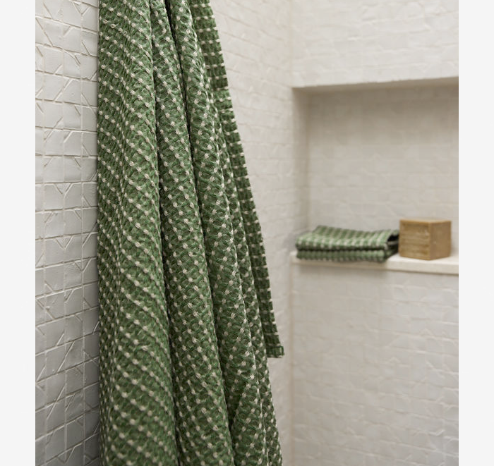 Green patterned towel hanging on a shower door with a white tiled wall in the background.