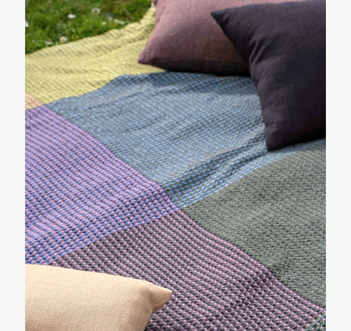 Multicolored woven blanket with pillows on a grassy background