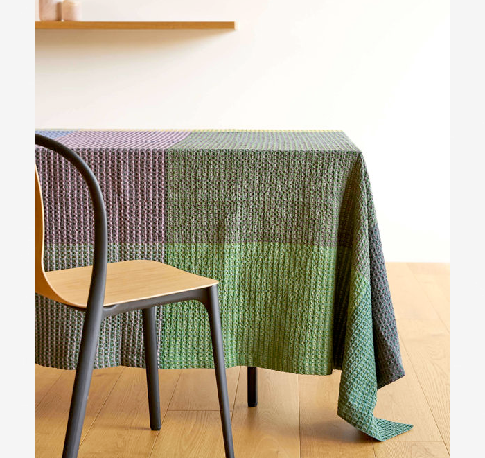 Colorful knitted tablecloth on a wooden table with a chair.