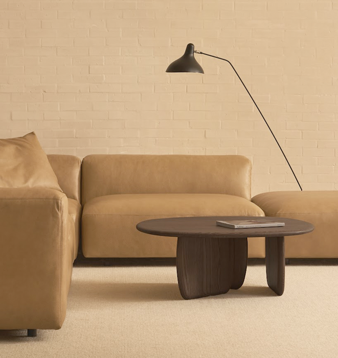 Beige sofa with a coffee table and floor lamp against a beige brick wall.