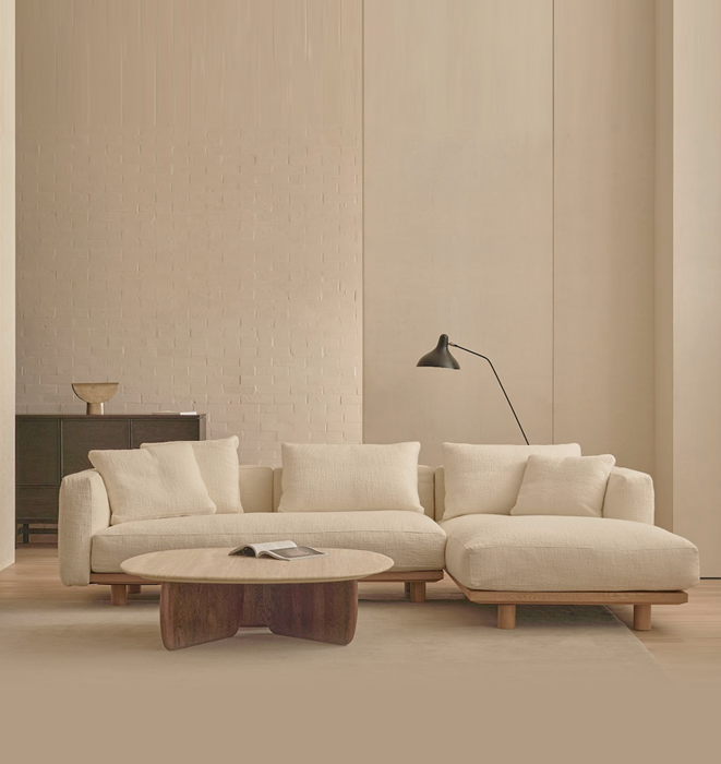 Beige sectional sofa in a minimalistic living room with a wooden coffee table and lamp.