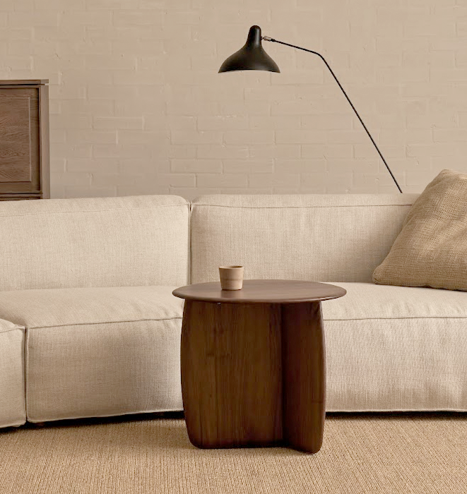 Modern living room with a beige sofa, wooden side table, and black floor lamp.