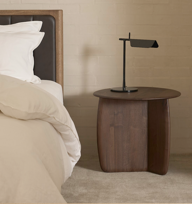 Wooden side table with a lamp next to a bed in a bedroom setting