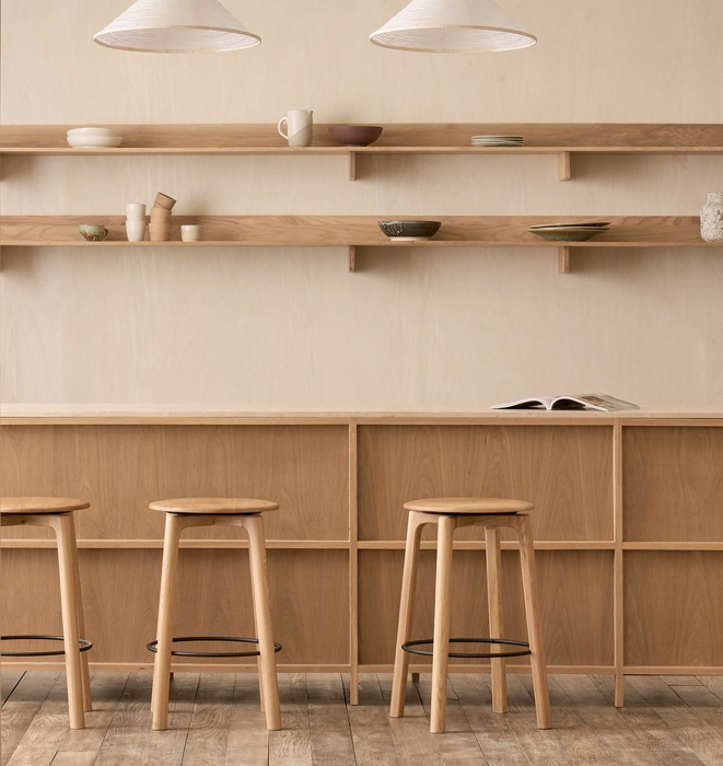 Wooden bar stools in front of a wall with shelves and a counter.