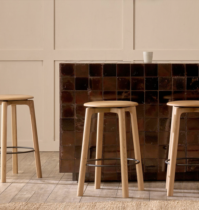 Three wooden stools in front of a tiled wall.
