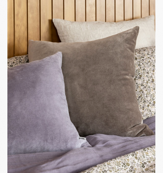 Three pillows in gray, purple, and beige on a bed with a wooden headboard.