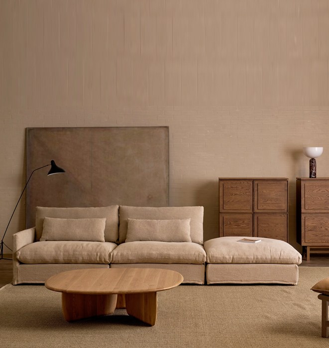 Beige sofa in a room with wooden furniture and a lamp against a beige wall.