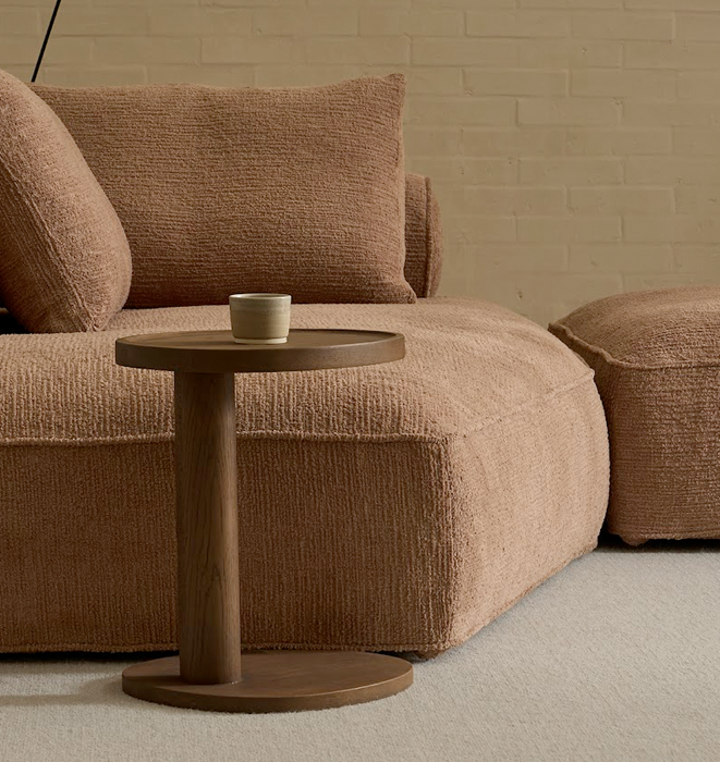 Brown textured sofa with a matching side table and a small ceramic cup on a neutral background