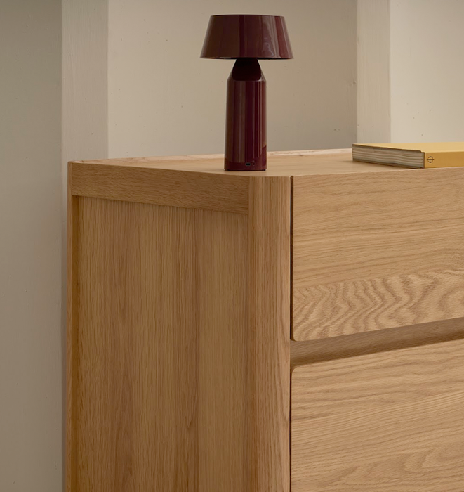 Wooden dresser with a lamp on top against a neutral wall