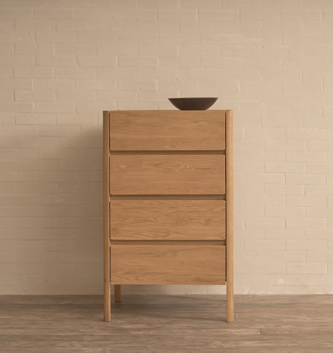 Wooden dresser with four drawers against a beige brick wall.