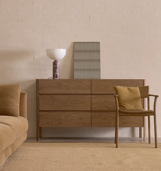 Wooden dresser with a chair and lamp in a room with beige walls and carpet.
