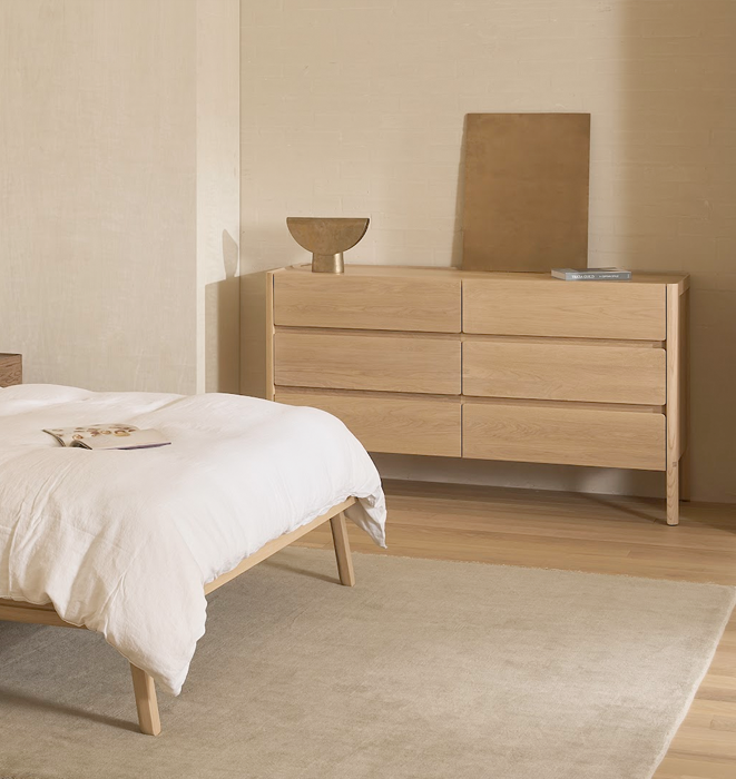Bedroom with wooden bed and dresser against a beige wall.