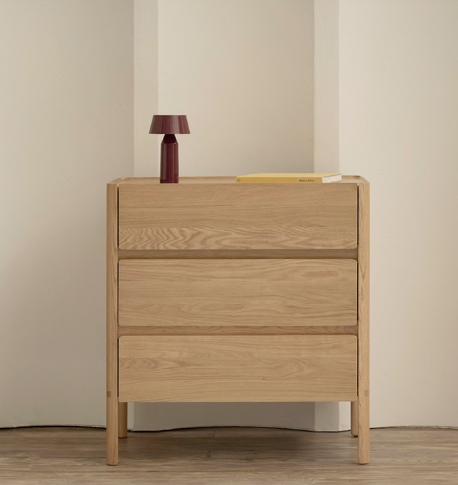 Wooden dresser with three drawers against a beige wall.
