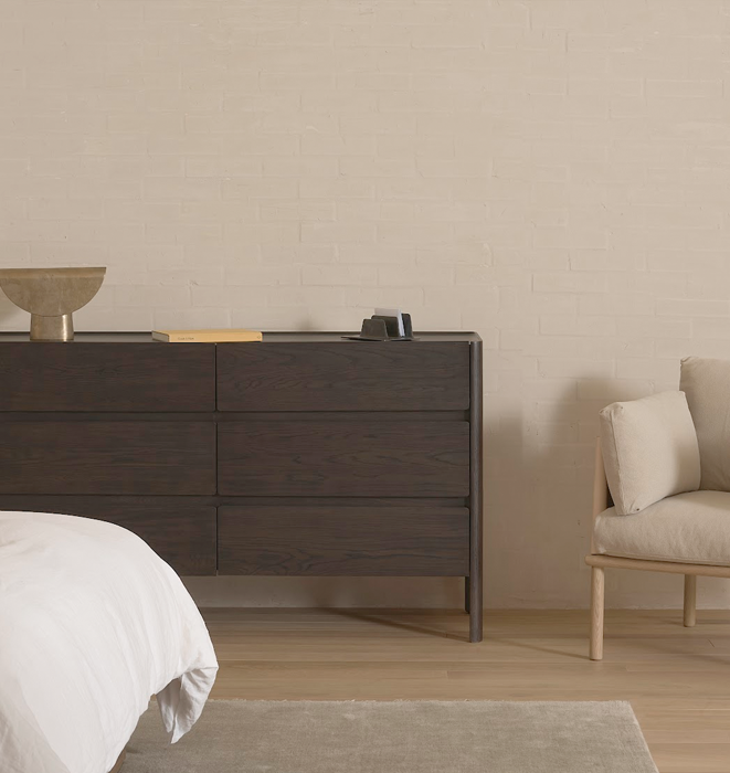 Wooden dresser in a bedroom with a beige wall and chair.