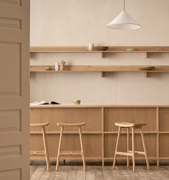 Wooden shelves with minimal decor against a beige wall, featuring three stools in front.