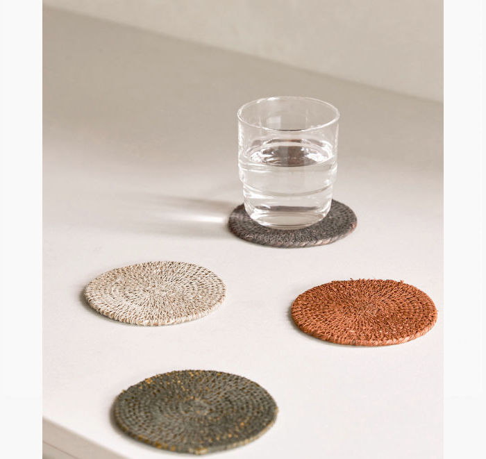 Set of four woven coasters on a white surface with a glass of water.