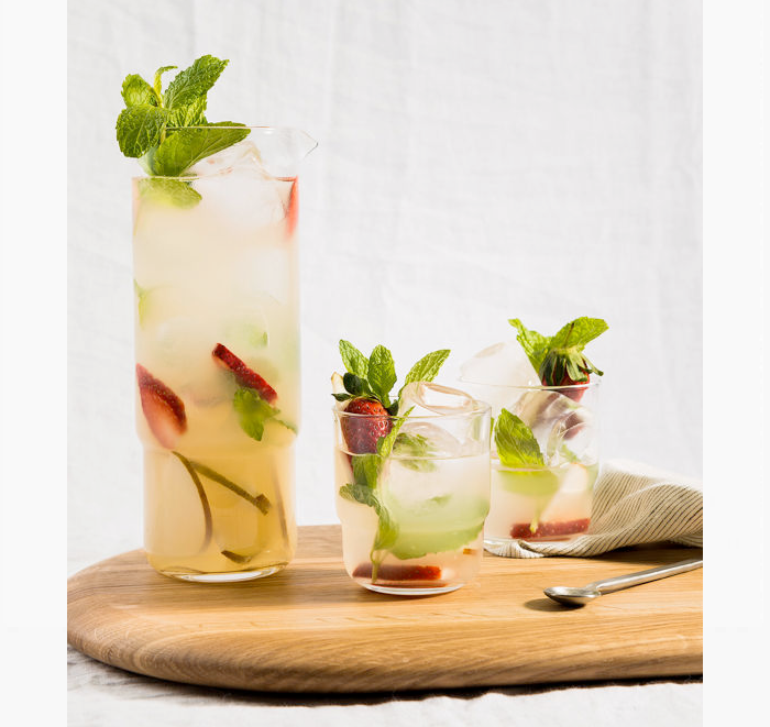 Three glasses of iced beverages with fruit and mint leaves on a wooden board.