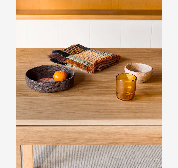 Wooden table with decorative items including a bowl, orange, folded fabric, and glass.