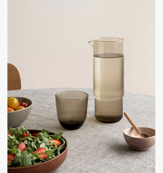 Table setting with a pitcher, glasses, and bowls on a neutral background