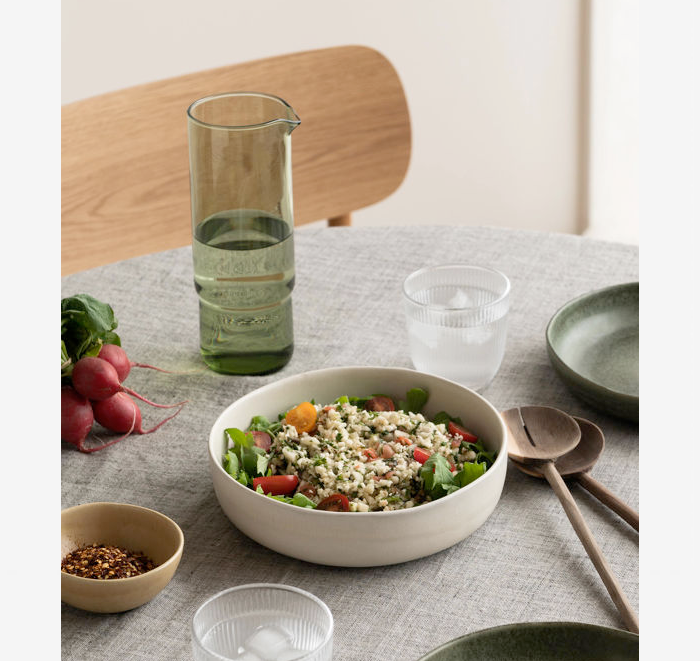 Salad bowl with salad on a table with a glass of water and utensils.